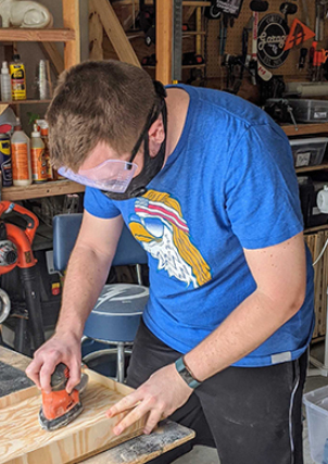Devin sanding a piece of wood on his workbench